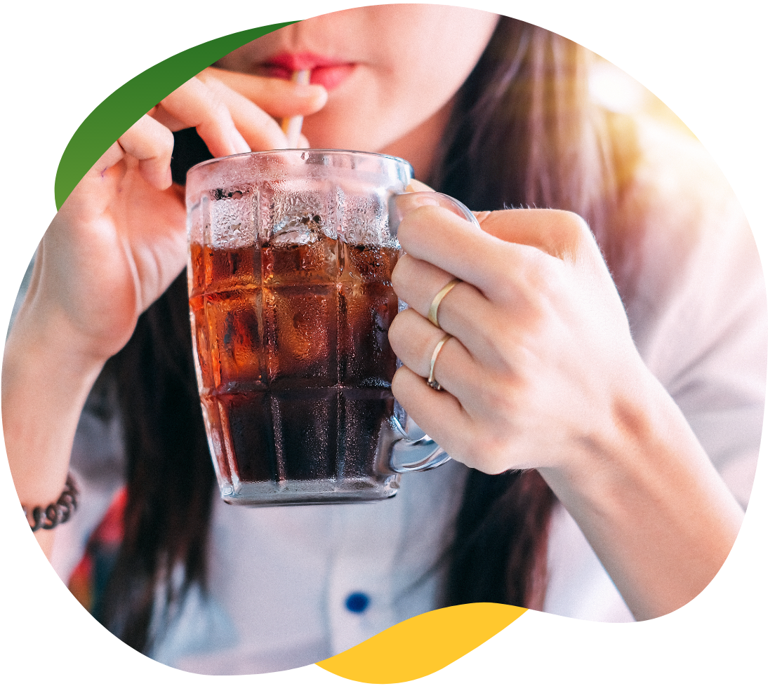 Wheat field in the bright suA young woman with long, brown hair holds a tall glass with her hand and drinks a carbonated drink with a straw out of it n