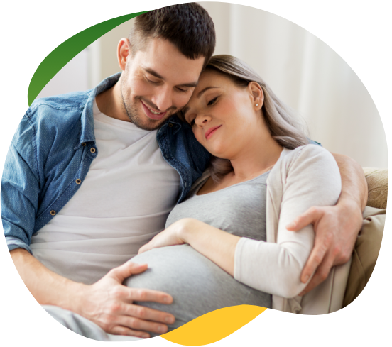 A pregnant woman suffering from bloating, sitting on the sofa with her eyes closed. Her partner comforts her and holds her in his arms